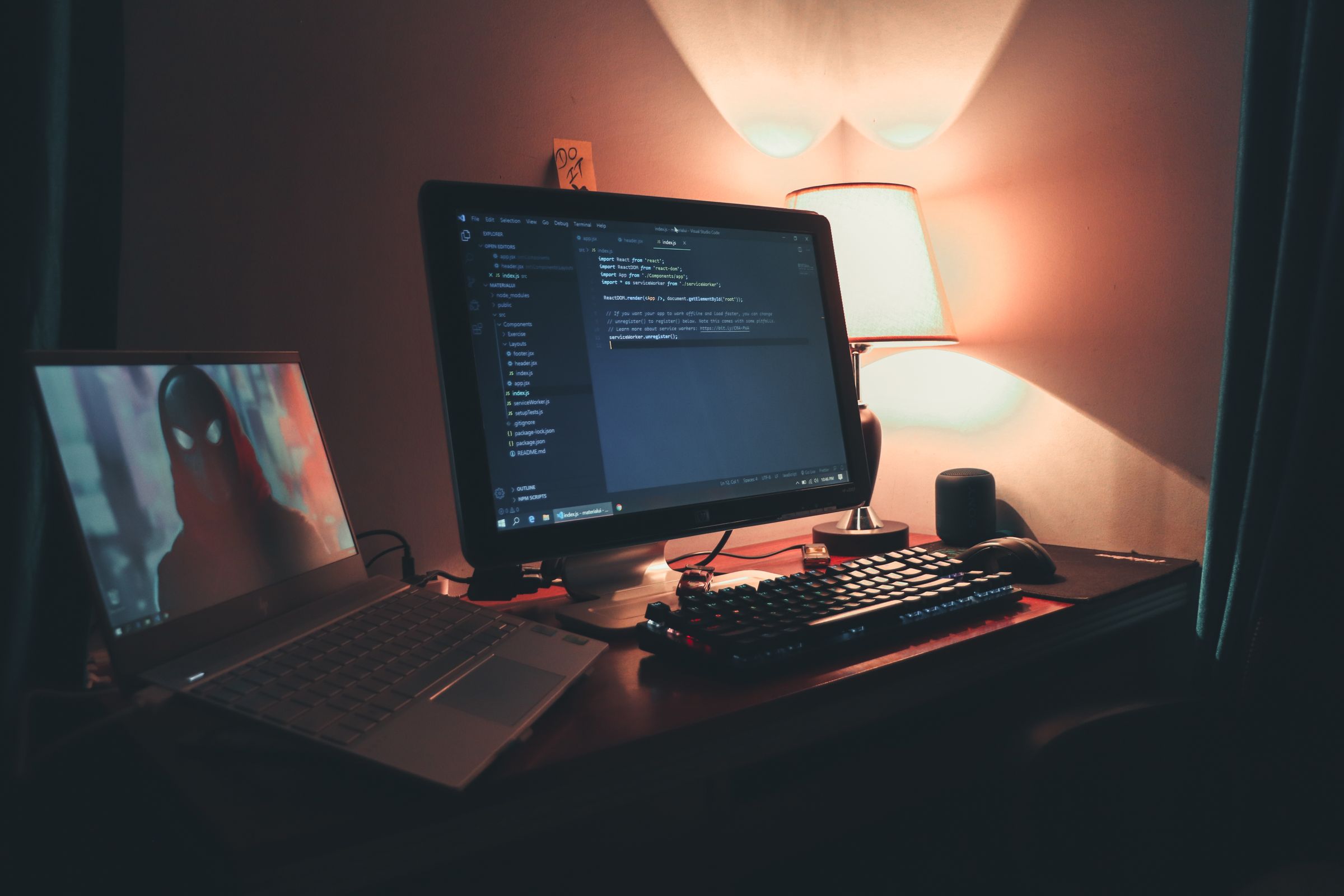 A desk in the dark, lit only by a monitor with code open and a sticky note that reads "DO IT": the product keeps running while no one is watching.