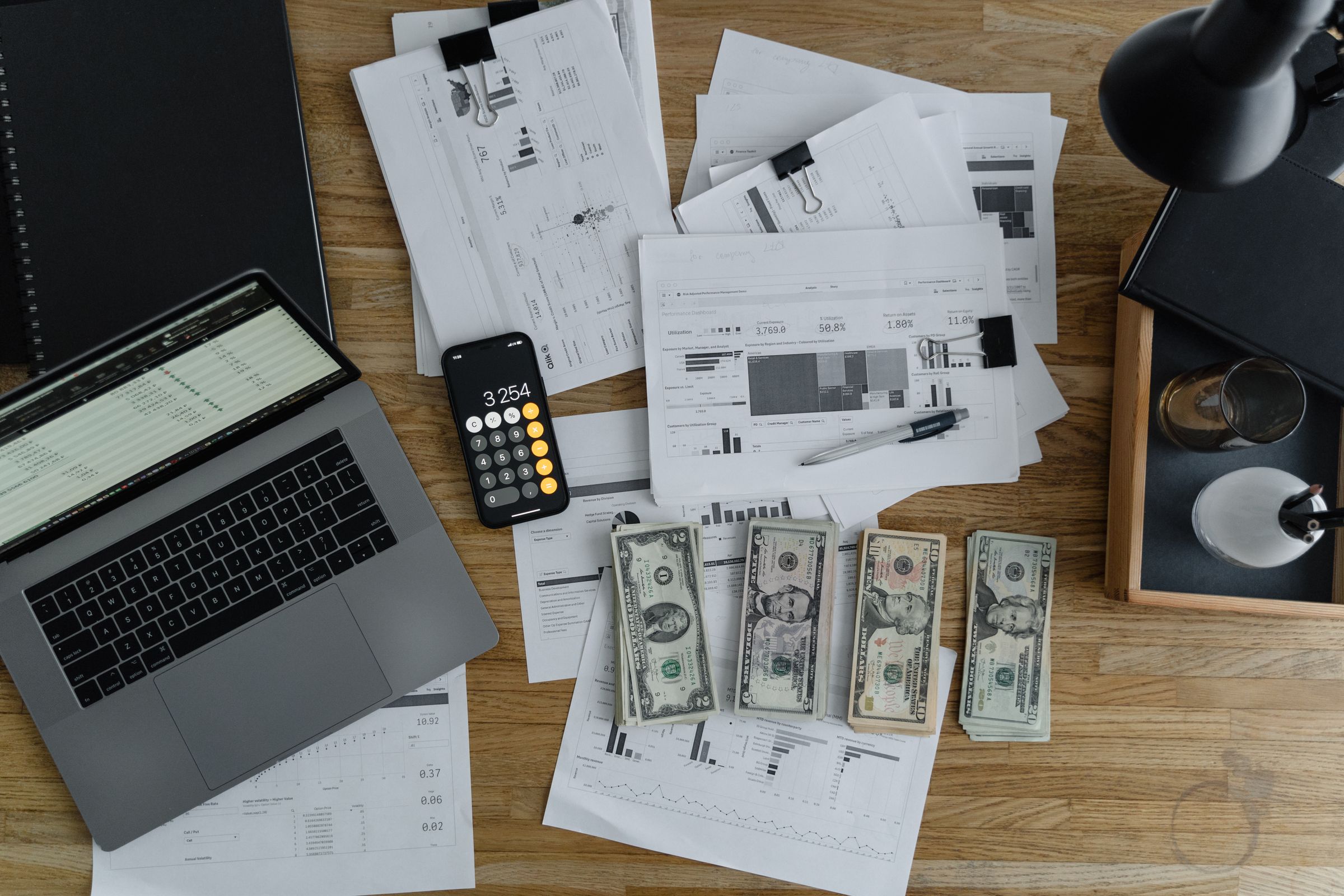A laptop, financial reports, and cash on a desk: the numbers a deal gets weighed by.